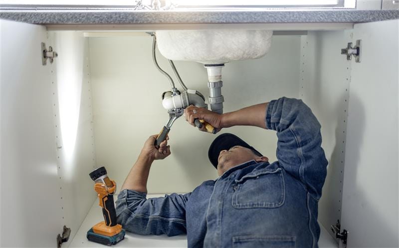 Plumber repairing pipes beneath a bathroom sink in North Port
