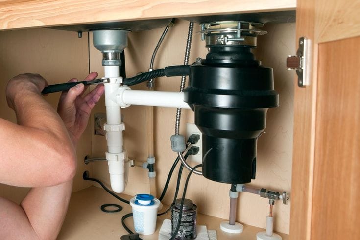 Plumber installing a garbage disposal beneath a kitchen sink in North Port