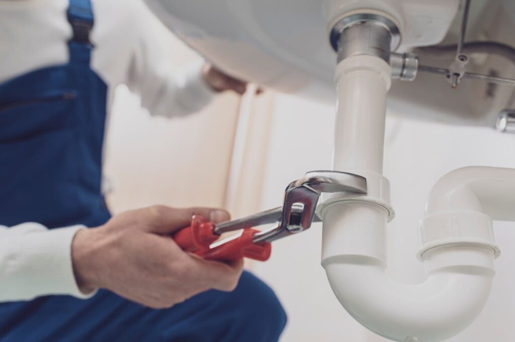 Plumber repairing a white drain pipe beneath a sink in North Port