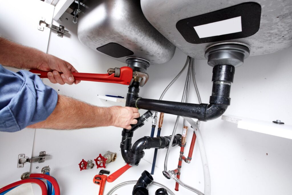 Plumber repairing drain pipes beneath a kitchen sink in North Port